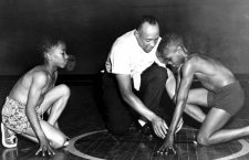 America's great Olympic track star Jesse Owens is showing two boys from the South Side Boys Club the starting position that brought him fame. Rajah Latimore (left) Sherman Davis 1st July 1954